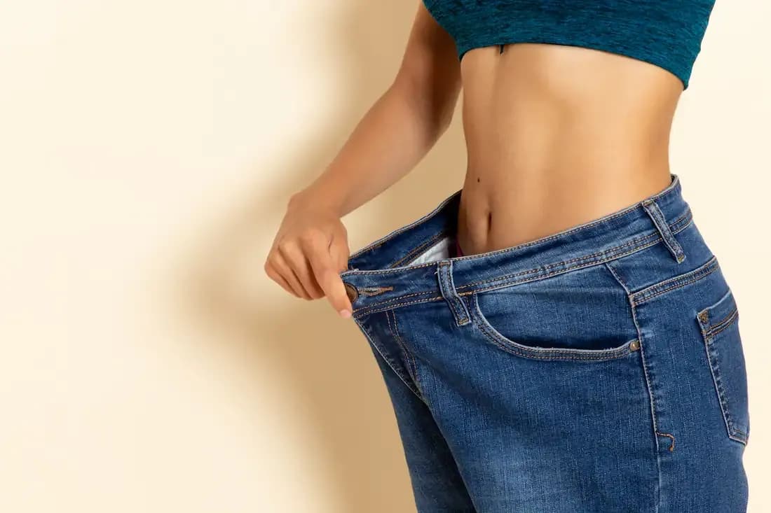 A fairly fit woman in jeans checking her waistline