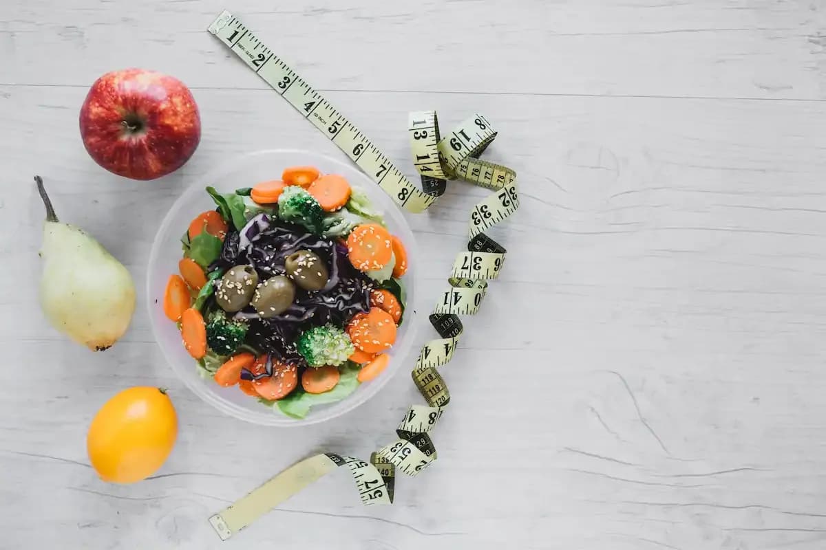 A coil of measuring tape laid out right next to a bowl of salad and several fruits
